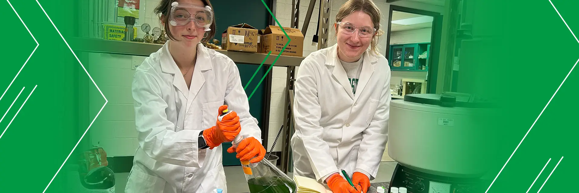 two women in safety goggles, gloves and lab coats work with chemicals