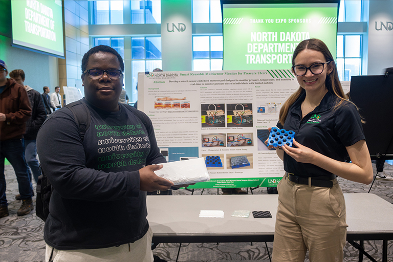 two students pose with their research project and poster at the senior design expo in 2025