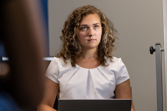 a student looks at a board while holding a laptop computer on their lap