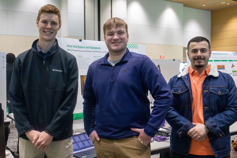 three students pose in front of a project display