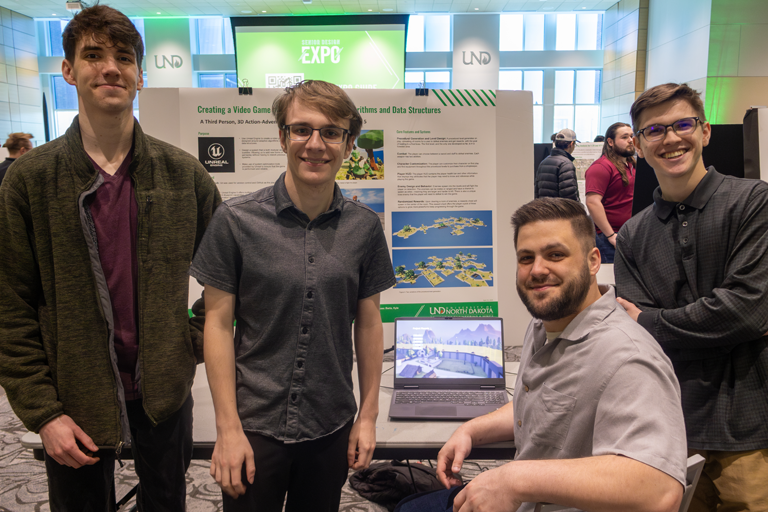 four students pose with a laptop showing a video game they designed