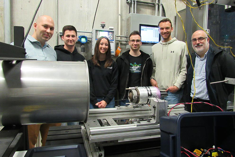 students and a professor pose with a rocket engine