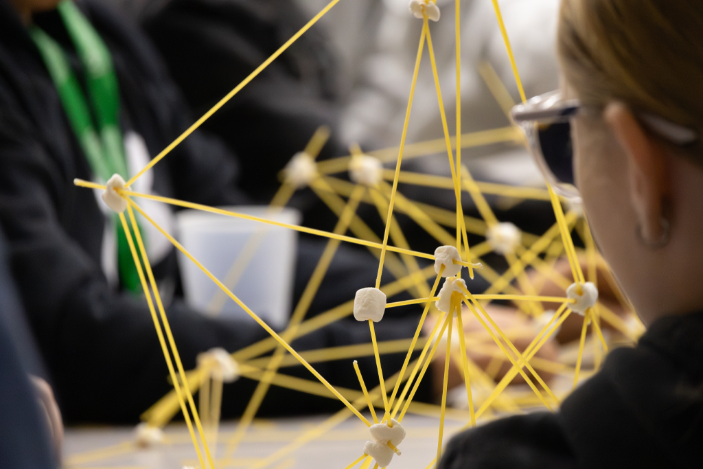 a young person builds a structure from pasta and marshmallows