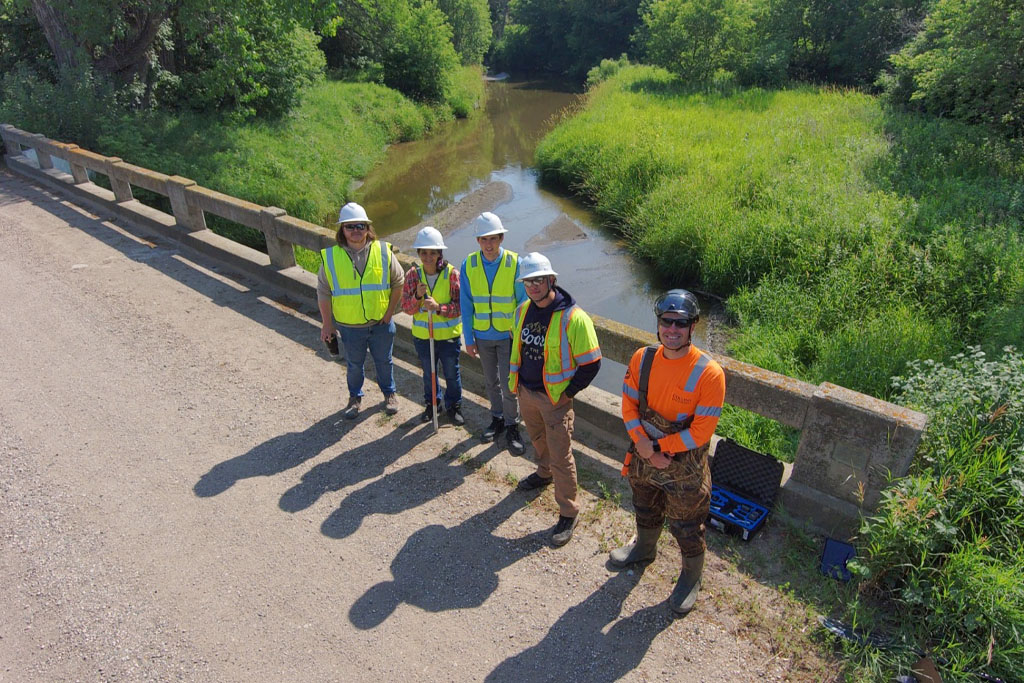 a group of people in hard hats and safety vests stand on a bridge with a river in the background